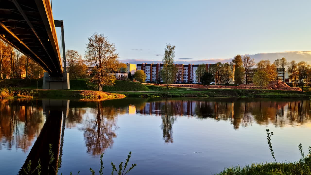Riverbank view of Gauja river from under pedestrian bridge in Valmiera, Latvia with reflections