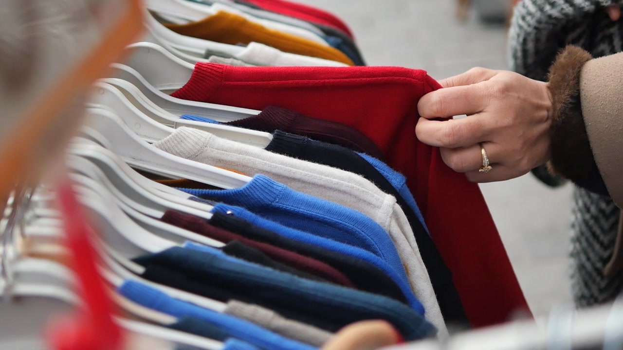 Close-up of a Hand Browsing Colorful Clothes on Hangers