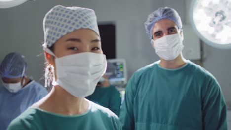 video of asian female surgeon in face mask and diverse colleague talking and smiling in theatre