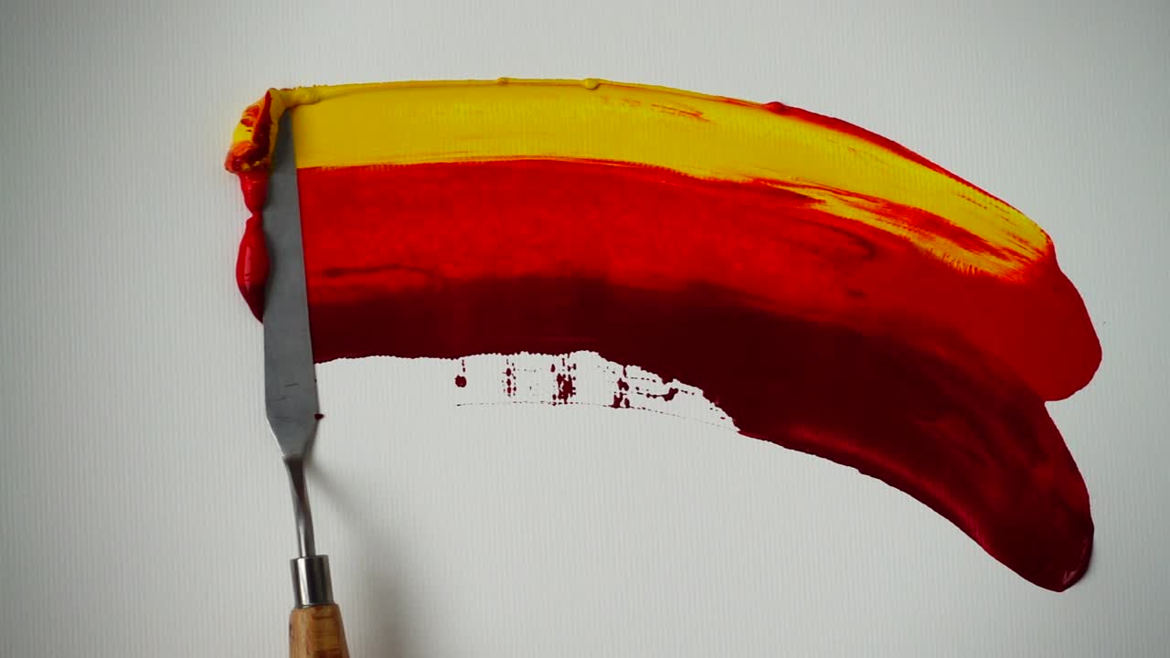 Spatola che stende pittura rossa e gialla su tela bianca