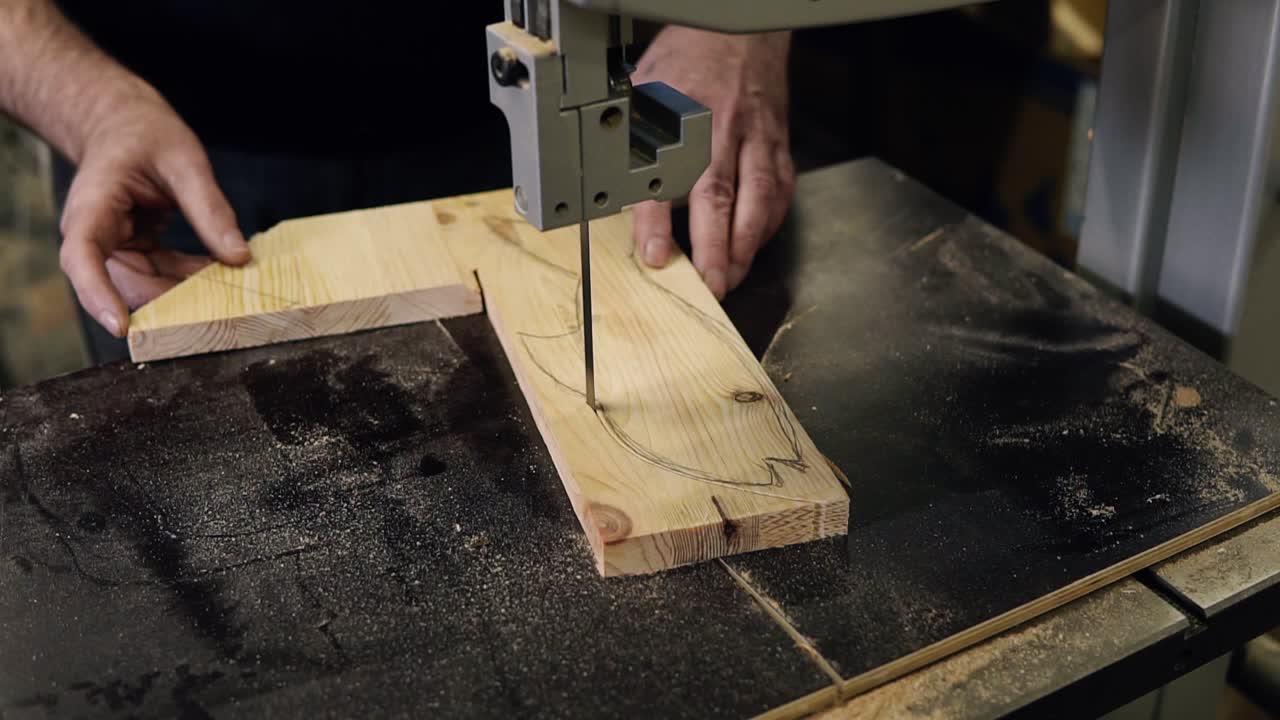 Close up footage of male's hands working with an electric cutting machine. High angle footage of a man cutting a fish shape wooden pattern on a table