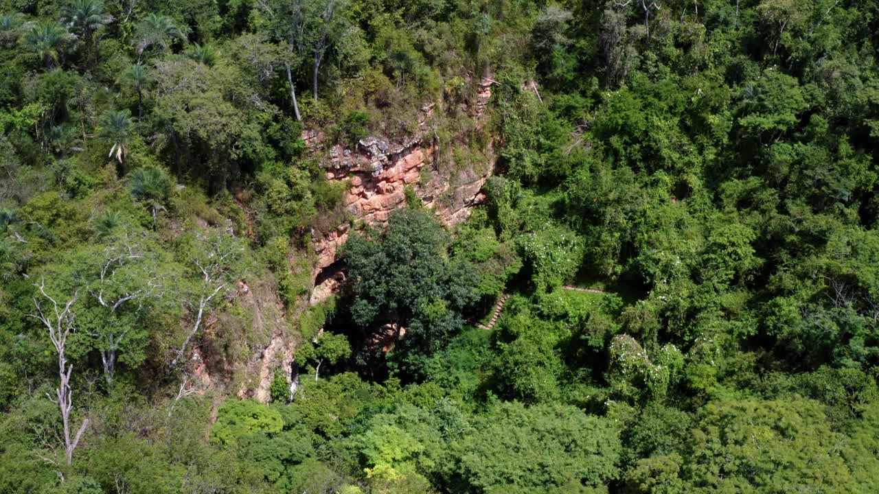toma aérea de drones giratorios de la entrada de la cueva al pozo encantado o poço encantado rodeado de árboles tropicales, plantas y acantilados en el parque nacional chapada diamantina en el norte de brasil-1