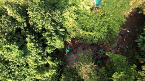 An-Aerial-view-of-a-river-cleaning-to-remove-plastic-in-Canggu,-Bali,-with-workers-in-green-surrounding-amidst-dense-foliage-and-trees