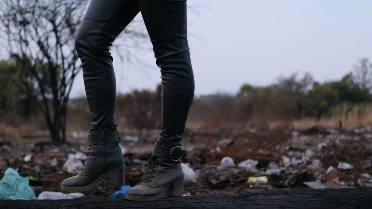 Ragazza con stivali che cammina su un tronco in una discarica