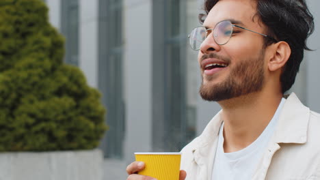 happy indian man enjoying drinking morning coffee hot drink relaxing taking a break in city street