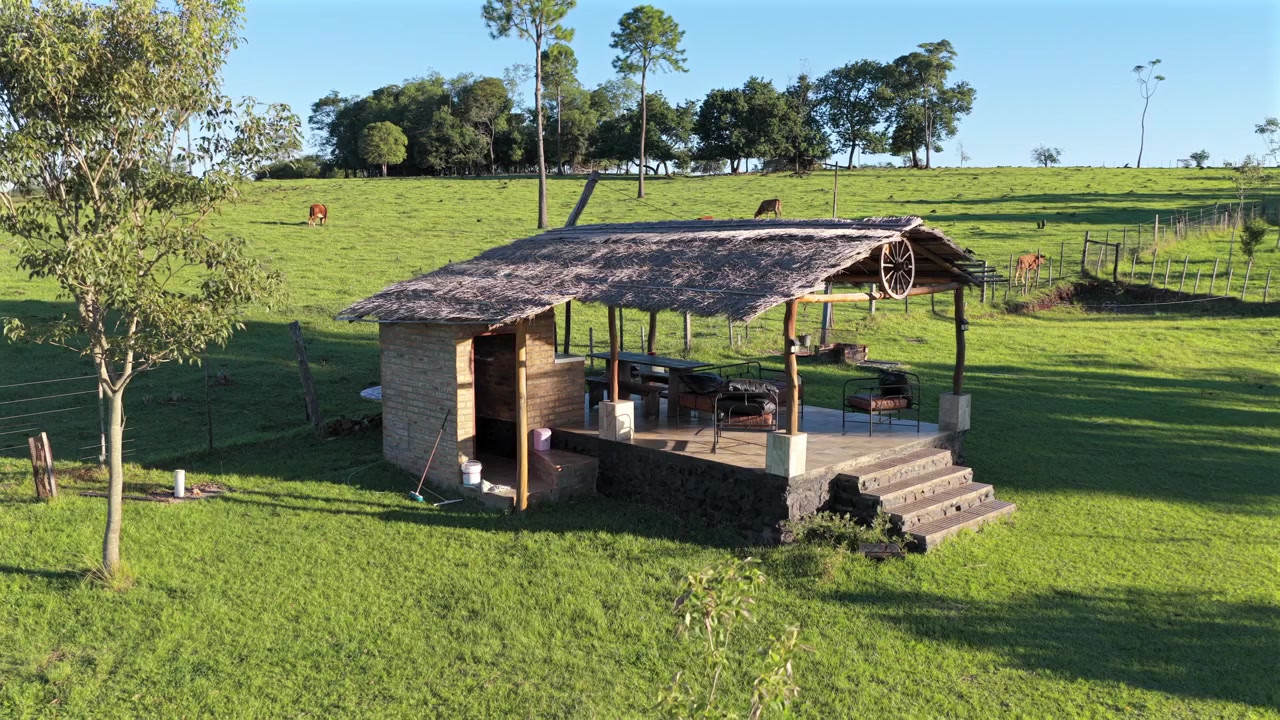 Un chiosco rustico con tetto di paglia si erge in una vasta fattoria verde. Adatto per promozioni di turismo rurale o per l'agriturismo