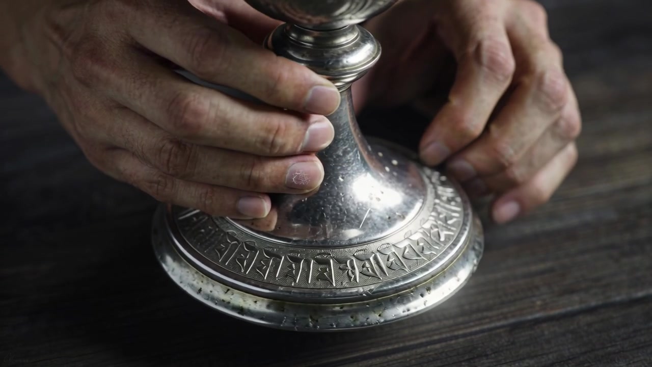 Mani adulte che ruotano la base di un calice d'argento su un tavolo di legno scuro, centrandolo per rivelare le vaiolature.