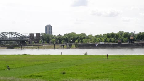 Hombre-Volando-Una-Cometa-Rápida-Y-Colorida-En-Un-Parque-De-La-Ciudad-De-Colonia,-Alemania,-En-Un-Soleado-Y-Ventoso-Día-De-Primavera