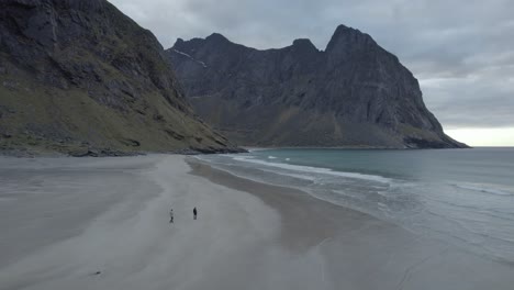 Luftaufnahme-Von-Menschen,-Die-Am-Strand-Von-Kvalvika-Spazieren-Gehen,-Auf-Den-Bewölkten-Lofoten,-Norwegen---Verfolgung,-Drohnenaufnahme