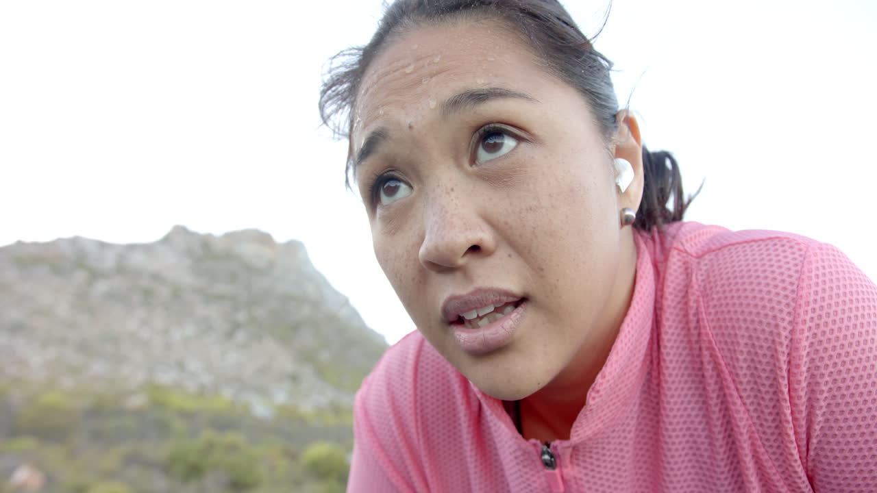 Exercising outdoors, woman wearing pink jacket and earbuds during mountain hike