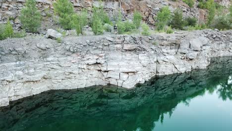 rocky cliff reflects in green water and tourist in summer clothes looking into it. natural landscape in the mountains outdoors. camera moves bottom top.