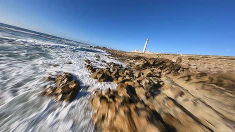 increíble drone fpv bajo sobre las olas del océano rocas para pasar el faro en la costa