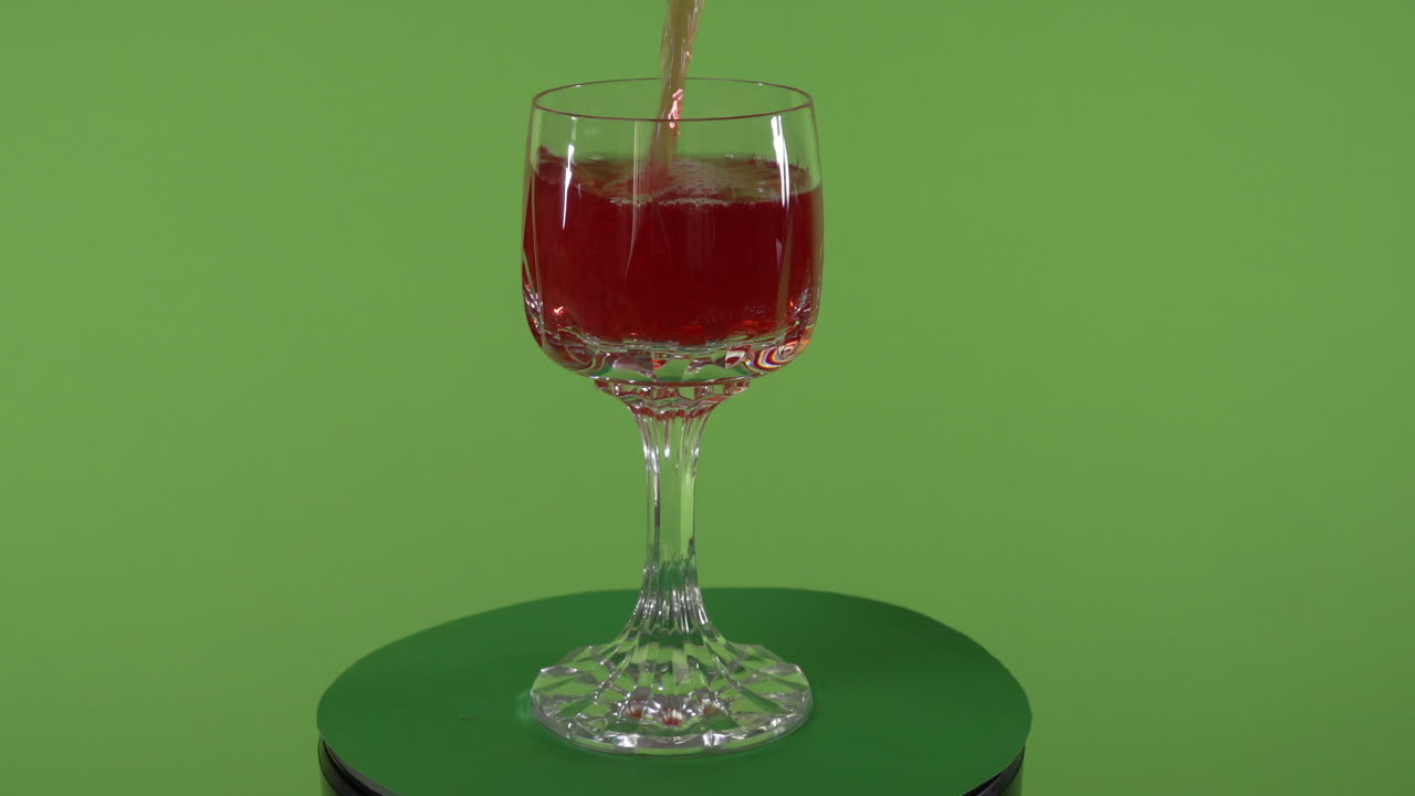 liquido rosso che si versa in un fantasioso bicchiere rotante davanti allo schermo verde chroma