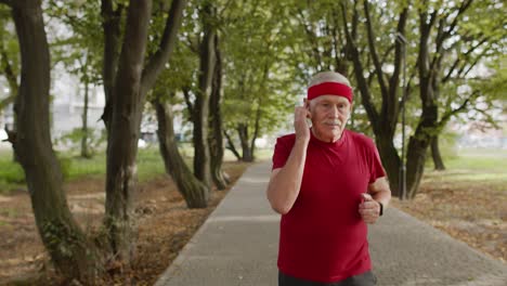 Älterer-Alter-Mann-Läuft,-Trainiert-Cardio-Im-Park-Und-Benutzt-Bluetooth-Kopfhörer,-Hört-Musik