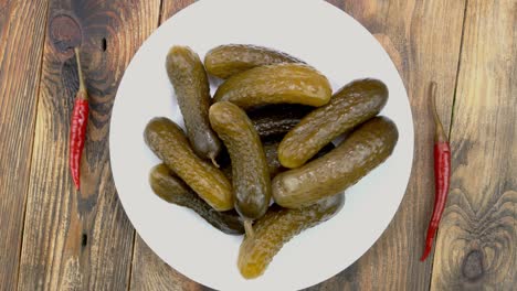 homemade salted cucumbers with chili pepper rotates in plate on wooden background.