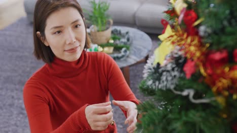 Video-of-happy-asian-woman-decorating-christmas-tree-at-home