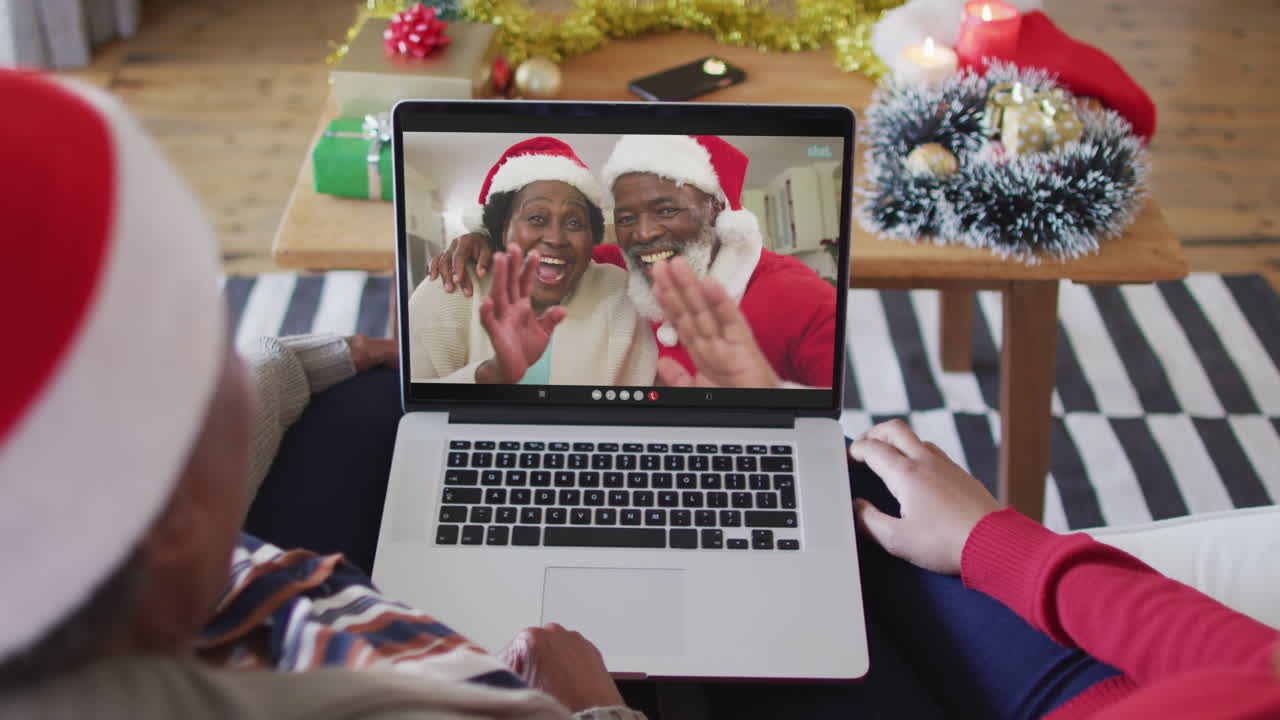 madre y hija afroamericanas usando una computadora portátil para una videollamada de navidad con la pareja en la pantalla