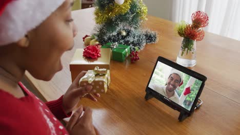 Afroamerikanische-Frau-Mit-Weihnachtsmütze-Nutzt-Tablet-Für-Weihnachtsvideoanruf-Mit-Mann-Auf-Dem-Bildschirm