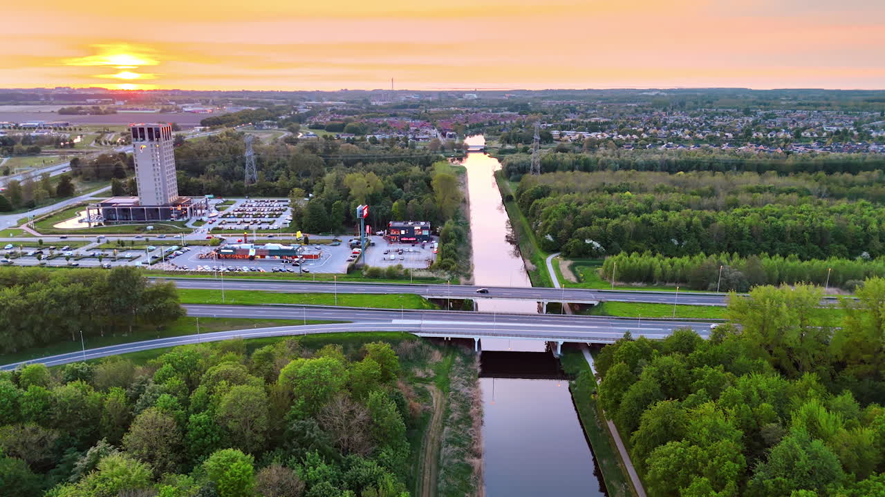 Canal sunset and greenery. A beautiful sunset casts warm hues over a canal surrounded by trees, with a bridge and highway in view