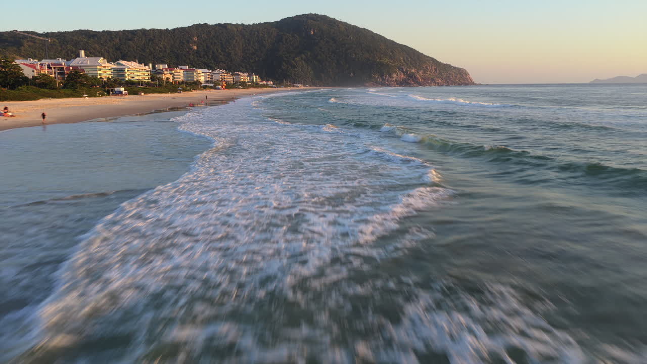 Vista aerea con drone dell'alba sulla spiaggia di Praia Brava a Florianopolis, Brasile, con onde che si infrangono sulla riva sabbiosa