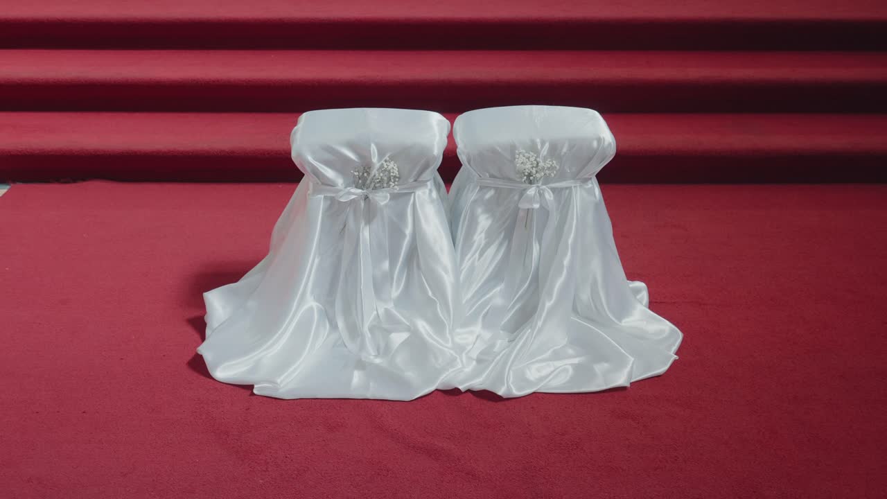 Sillas de boda blancas cubiertas descansando sobre una alfombra roja dentro de una iglesia tranquila