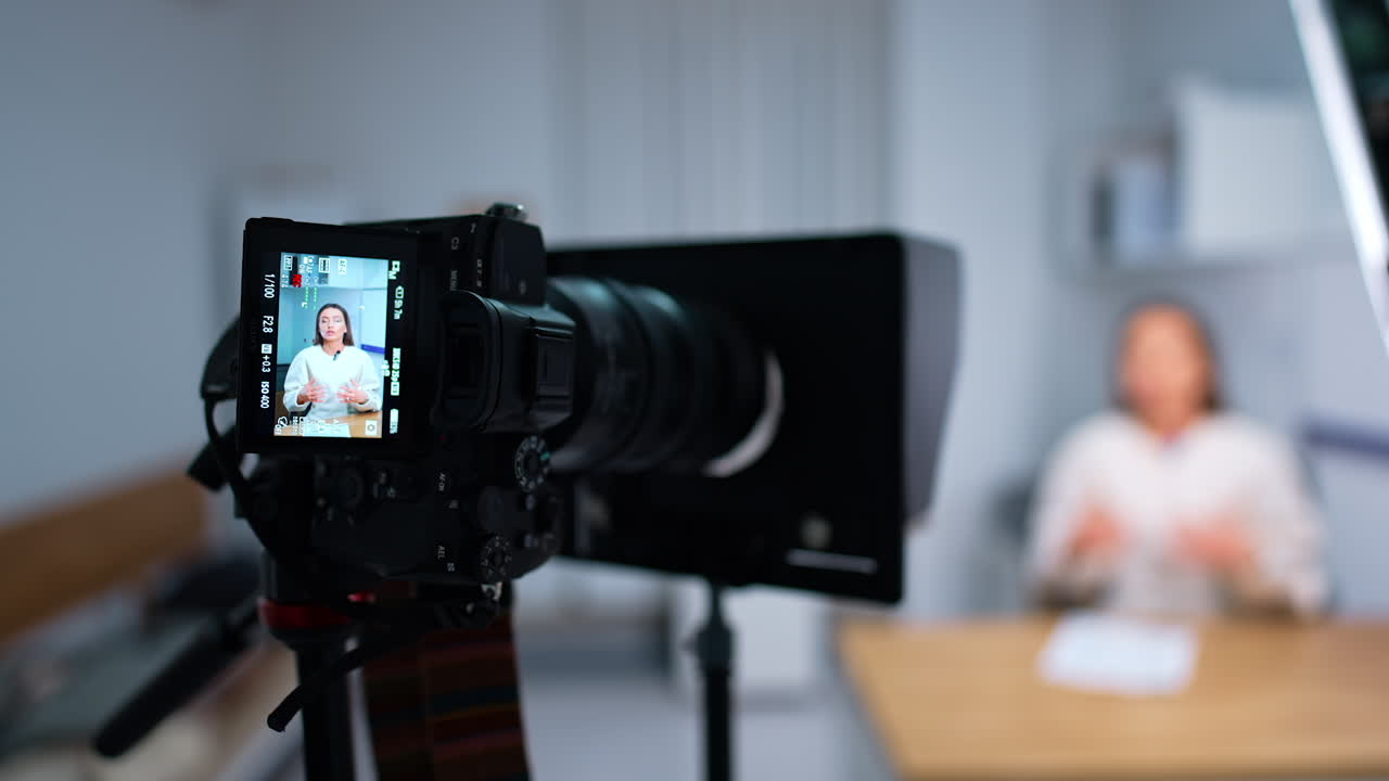 Long-haired woman giving a speech recorded by camera. Close-up view of a display on professional camera. Blurred backdrop.