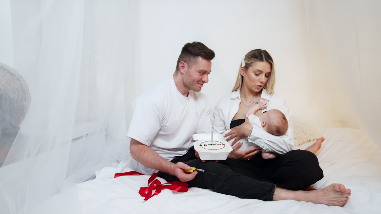 Happy parents celebrating the second month of their first newborn child. Smiling dad lights the candle on the festive cake.