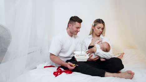 happy parents celebrating the second month of their first newborn child. smiling dad lights the candle on the festive cake.