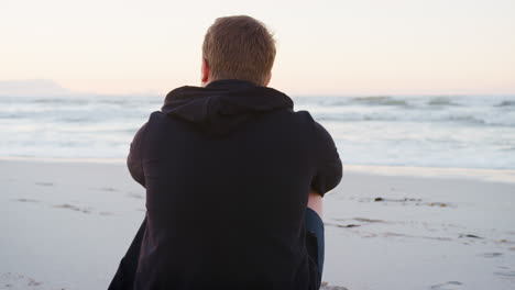 rear view of young man on beach watching sun rise over ocean