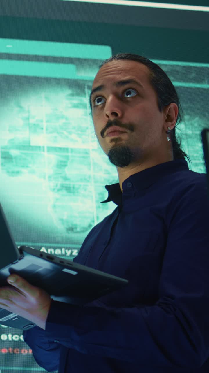 Man Working on Laptop in High-Tech Control Room with Digital Screens