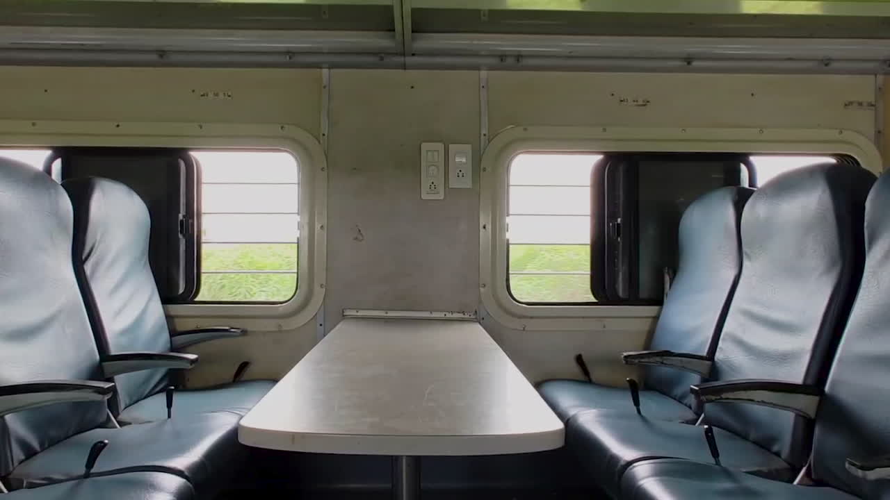 Camera moves forward, face-to-face seating arrangements in economy class of moving Indian train, dynamic and communal atmosphere of train travel in India.
