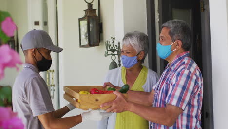 una pareja biracial y un repartidor de comida en la puerta con máscaras faciales.
