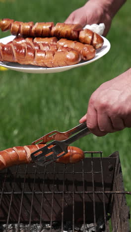 man on picnic prepares juicy sausages in barbecue. chef putting ready roasted hot dog sausages into a plate in the garden. vertical video
