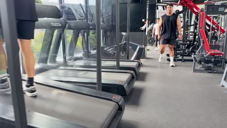 A man exercises on a treadmill in a well-lit, modern gym with large windows and various equipment