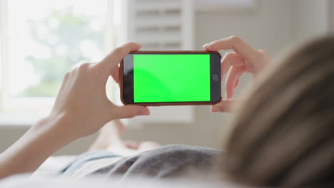 woman holding smartphone with green screen in bedroom