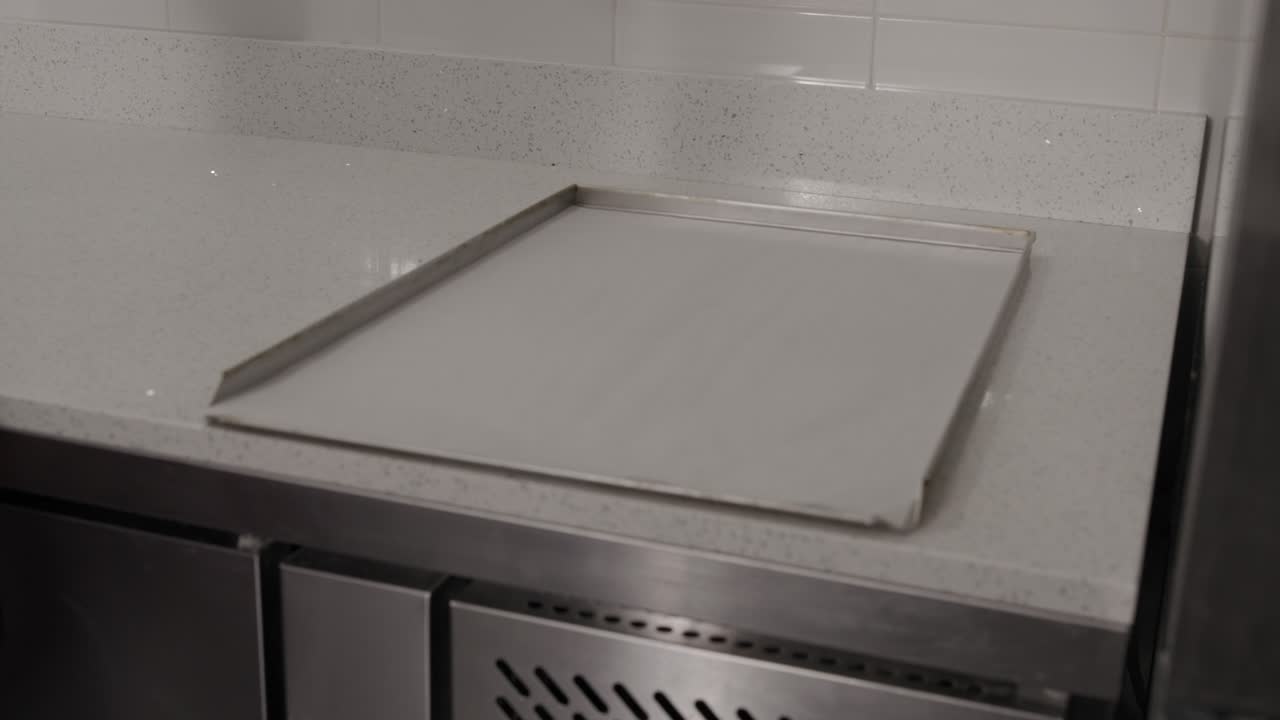 Man putting an empty baking tray with baking sheet on a worktop in an artisan pastry shop, 4K