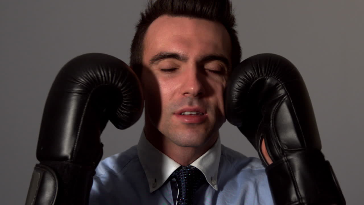 un hombre de negocios golpeándose la cara con guantes negros.