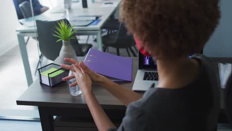 Mid-section-of-african-american-woman-using-hands-sanitizer-at-modern-office