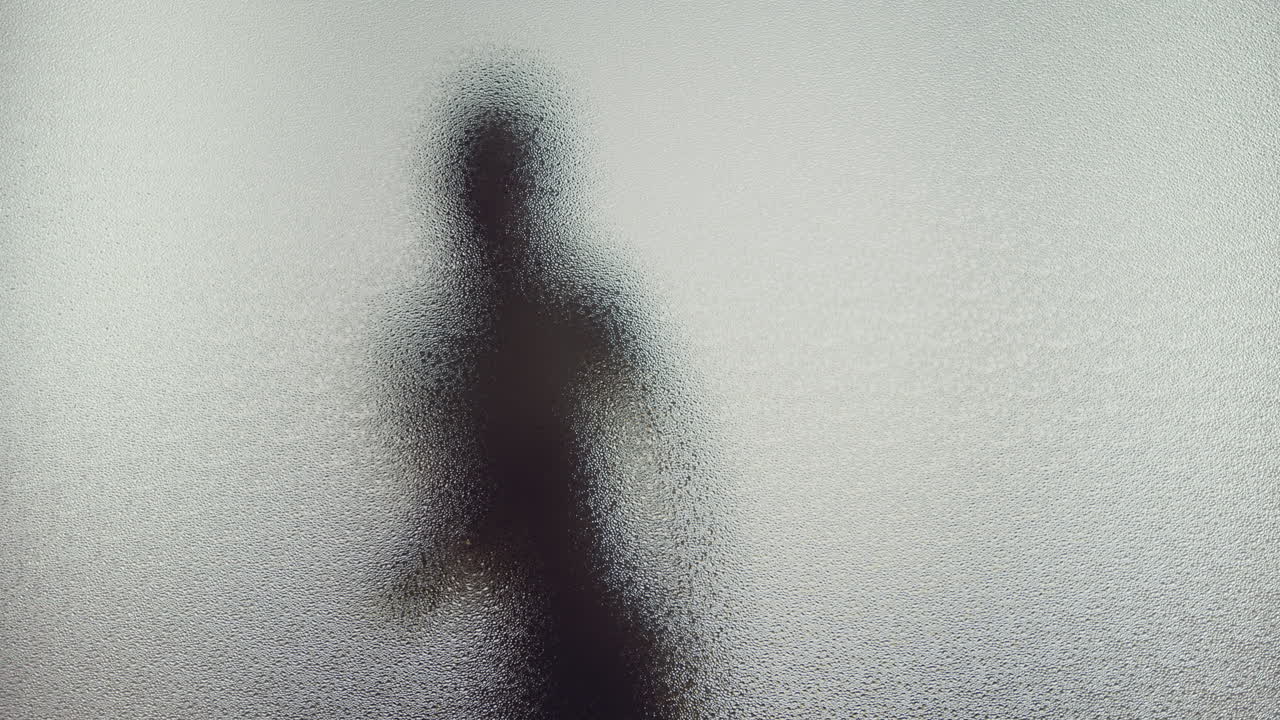 A female silhouette behind the frosted window dances slowly
