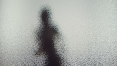 a female silhouette behind the frosted window dances slowly