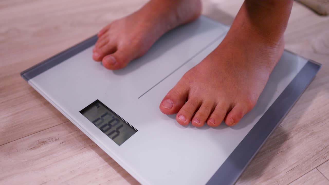 Close-up shot of bare feet stepping onto a digital scale to measure body weight