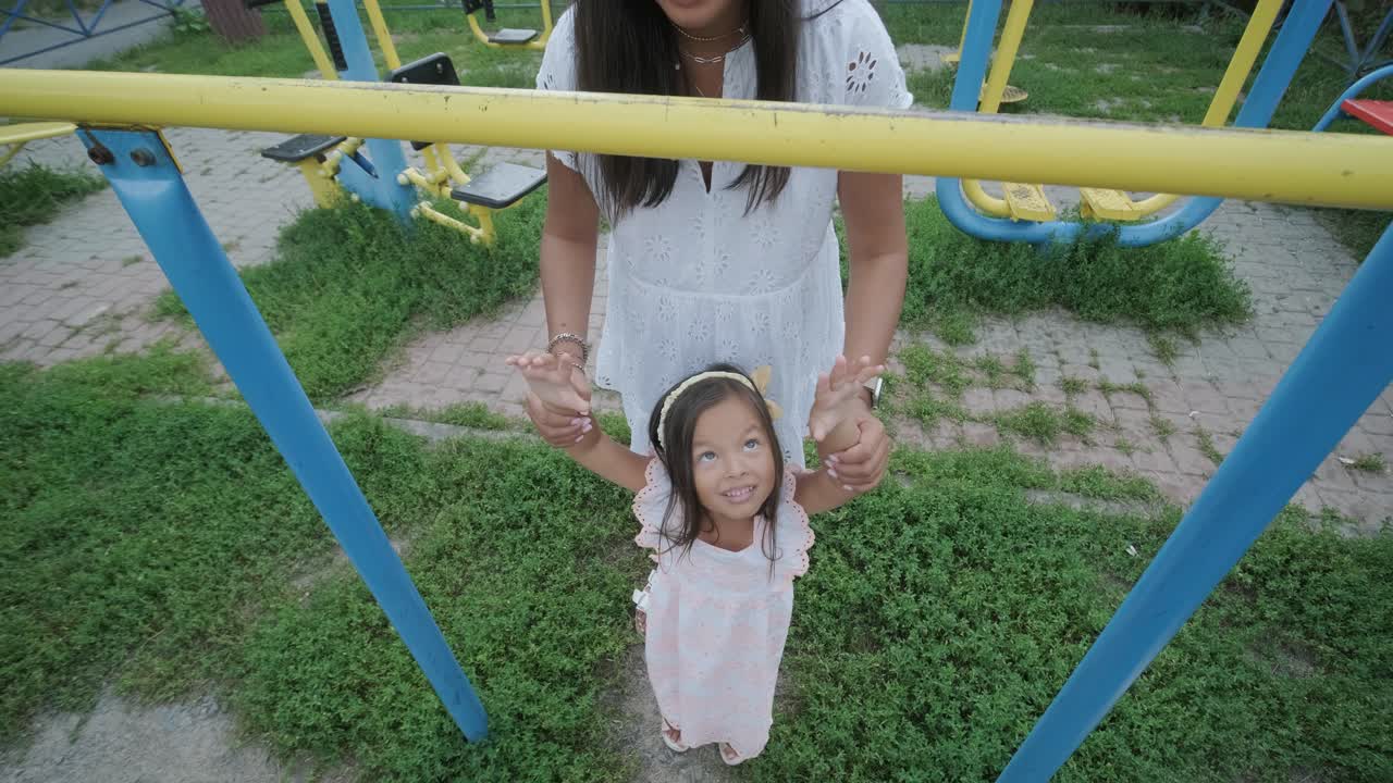 una madre embarazada y su hija joven disfrutan de un tiempo de juego juntos en un patio de recreo en el parque, rodeados de árboles y vegetación