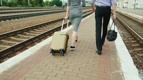 two business people walk along the railway with their luggage