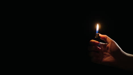 hand ignites flames on lighter on black background