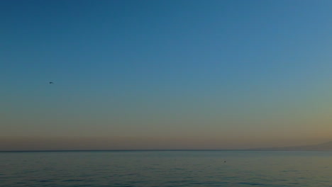 wide shot of a distant mountain with a blue sky transitioning into orange hues at the horizon over calm waters