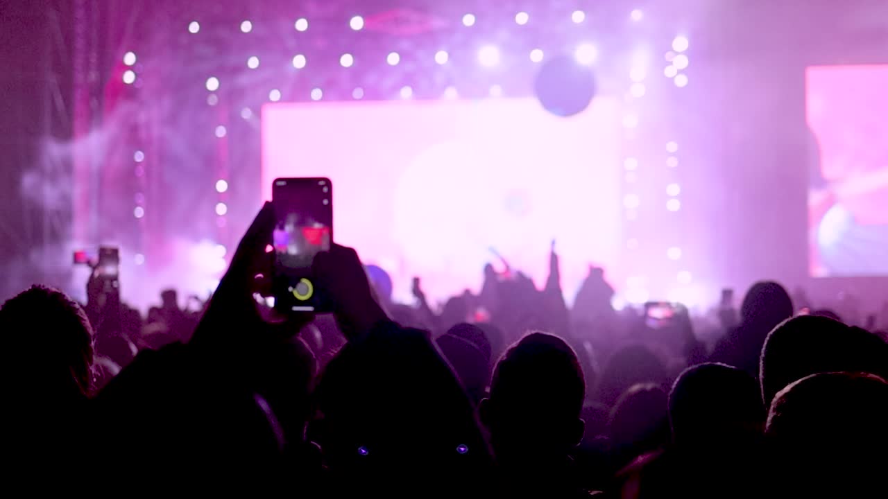 Folla di fan che ballano e filmano il palco e lo spettacolo di luci.
