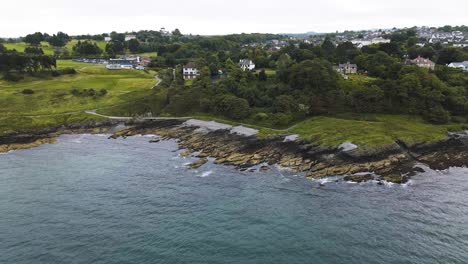 Reversing-and-rising-aerial-reveal-of-coastline-in-Crawfordsburn,-County-Down