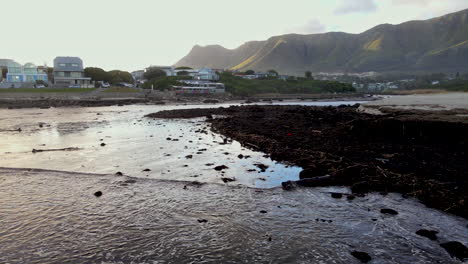 Drone-flight-over-small-waves-running-onto-beach-with-loads-of-river-debris-deposited-through-river-mouth-after-coastal-rain-storm