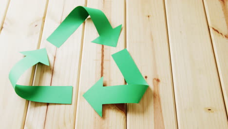 primer plano del símbolo de reciclaje de flechas de papel verde sobre fondo de madera, con espacio para copiar