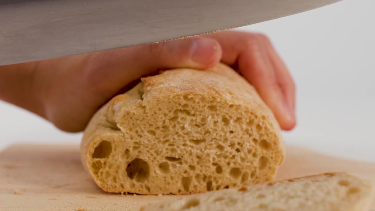 Primo piano di mani che usano un coltello da chef per affettare pane a lievitazione naturale croccante su legno.